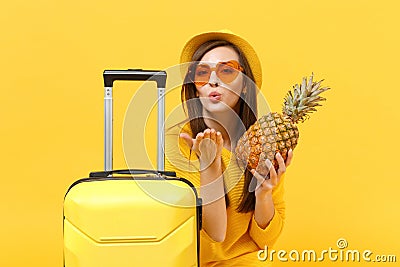 Traveler tourist woman in hat blowing sending air kiss hold fresh ripe pineapple fruit on yellow orange Stock Photo