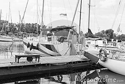 Traveler walking in river marina near of boats with folded sails. Young fashionable man start river journey by yacht. Man and Stock Photo