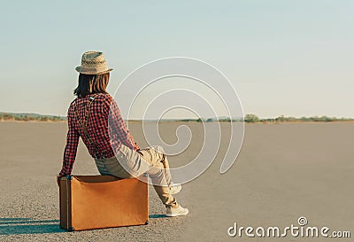 Traveler woman sitting on suitcase on road, copy-space Stock Photo