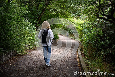 Traveler woman walks away in forest. Lonely girl hiker is alone on path in dark woods Stock Photo