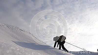 Travelers climb rope to their victory through snow uphill in a strong wind. tourists in winter work together as team Stock Photo