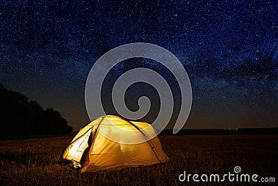 Traveling and camping concept - camp tent at night under a sky full of stars. Orange illuminated tent. Beautiful nature - field, Stock Photo