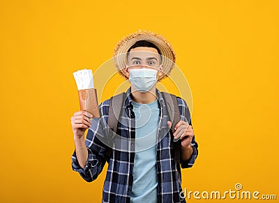 Traveling during covid. Young tourist with backpack wearing face mask, holding tickets and passport, orange background Stock Photo