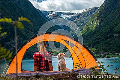 Traveling Norway, Young woman sits in the tent with her dog enjoying Beautiful view of Buerdalen Valley and Sandvevatnet Lake Stock Photo