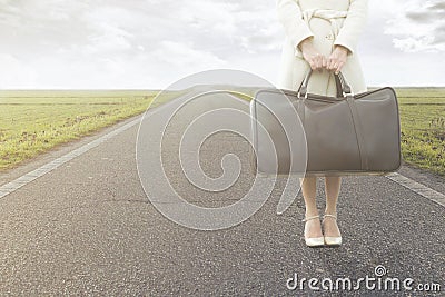 Traveling woman waits with her suitcase on the roadside Stock Photo