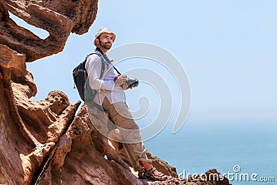 Traveller with camera sits on the edge of a cliff. Stock Photo