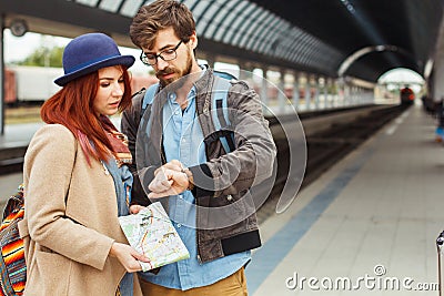 Hipster Traveller couple looking at smart watch while waiting for the train at railway station. Autumn time. Woman Stock Photo