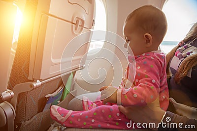 Travelling with infant. Mother and baby sitting together in airplane near the window in sunny day Stock Photo