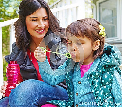 She treasures every fleeting moment. a mother watching her daughter blow bubbles outside. Stock Photo