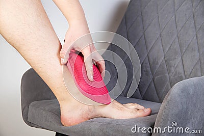 Treatment of pain and inflammation of the ankle joint with a heating pad with hot water. Removal of inflammation, thermotherapy, Stock Photo
