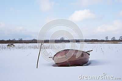 Tree and a boat stand on the shore of a snowy lake Stock Photo