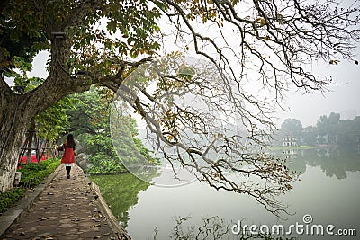 Tree in fall season at Hoan Kiem lake with Vietnamese girl wear traditional dress Ao Dai walking by lake in Hanoi Stock Photo