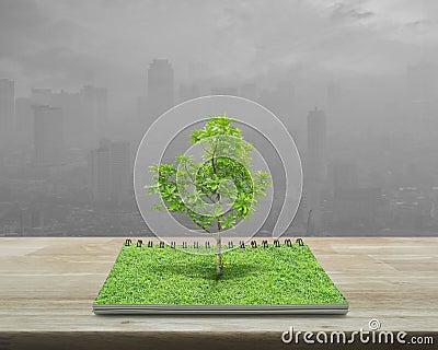 Tree growing from an open book on wooden table over pollution ci Stock Photo