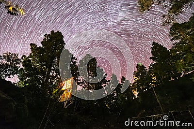 Tree house in the middle of nature under a circular spiral stars trail Stock Photo