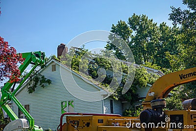 Tree service equipment is seen by a tree that had fallen on the roof of a house Editorial Stock Photo