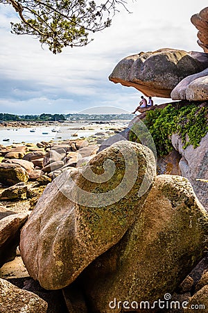 Two men sitting under a boulder are enjoying the view over the bay at low tide in Brittany, France Editorial Stock Photo