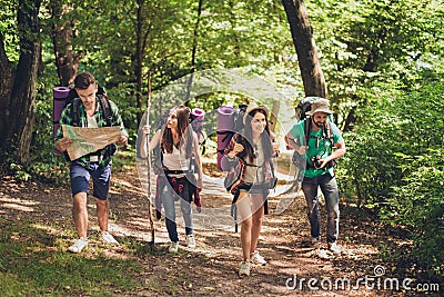 Trekking, camping and wild life concept. Four best friends are hiking in the spring woods, the guy is checking the route on a map, Stock Photo