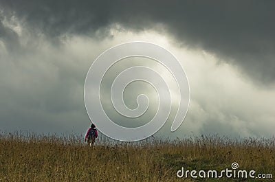 Trekking through prairie hillside under dark clouds Stock Photo