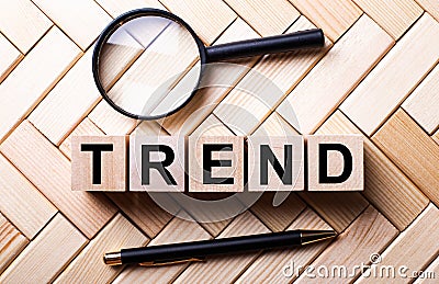 TREND word is made up of wooden cubes near a magnifying glass and a fountain pen on a wooden background. Marketing concept Stock Photo