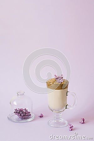 Trendy drink 2020 dalgon Coffee in a transparent Cup with a paper tube, a plate with lilac flowers on a lilac background with a Stock Photo