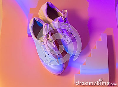Trendy fashion white sneakers on geometry podium on abstract bright background. Neon lights on casual shoes. Violet and orange Stock Photo