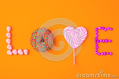 Trendy flat lay lettering. Inscription love by sweets on orange vivid background, isolated Stock Photo