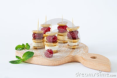 Trendy food skewers with mini pancakes, raspberry, banana and sugar powder isolated on white background Stock Photo