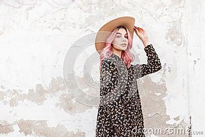 Trendy gorgeous young woman with chic pink hair in black stylish beautiful floral dress near wall on street. Lovely girl fashion Stock Photo