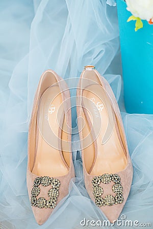 Trendy, graceful suede high heel shoes and wedding rings and jewelery in a blue suede chair. Wedding details. Stock Photo