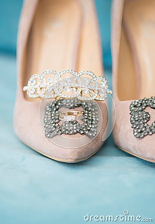 Trendy, graceful suede high heel shoes and wedding rings and jewelery in a blue suede chair. Wedding details. Stock Photo