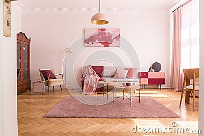 Trendy living room interior with grey couch with pastel pink pillows and blanket, stylish beige armchair with burgundy pillow and Stock Photo