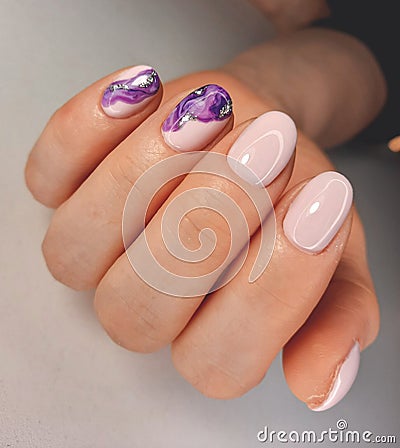Trendy pink gel nail polish with an abstract purple fluid design. Manicure of soft pink color with a beautiful spreading pattern. Stock Photo