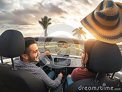 Trendy rich couple having fun driving convertible car at sunset - Happy romantic lovers enjoying their road trip in cabriolet auto Stock Photo