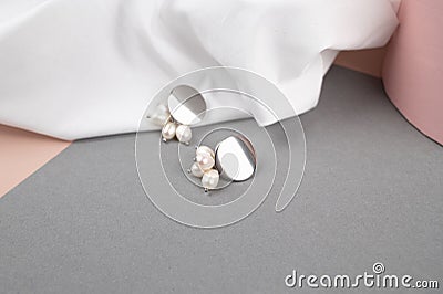 Trendy silver earrings over crumpled withe fabric background. Fashionable women& x27;s jewelry with pearls Stock Photo