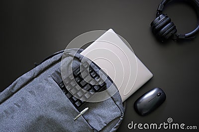 Trendy urban gray textile laptop backpack along with gadgets on a black. Silver laptop, mouse, headphones, pen and keyboard - Stock Photo