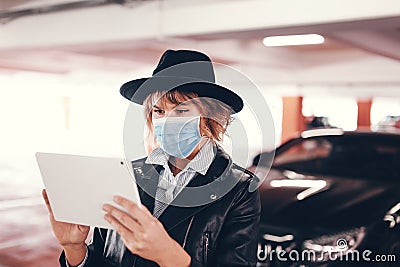 Trendy urban woman in mask typing on tablet at car Stock Photo