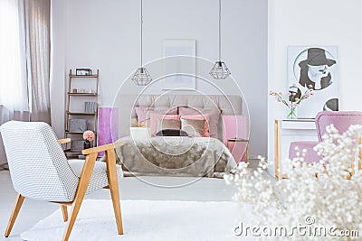 Vintage armchair in cute bedroom interior with black and white poster and king size bed with satin bedding Stock Photo