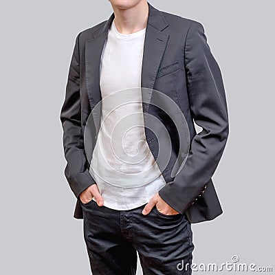 Trendy young man wearing grey blazer and dark jeans, standing against a grey background Stock Photo