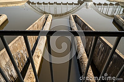 Triangle pattern of concrete structure of an irrigation control system with water and reflection of white concrete railroad bridge Stock Photo