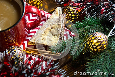 Triangular cookies with powdered sugar and cinnamon on a napkin with a zigzag pattern in the Christmas decor. Red coffee mug with Stock Photo