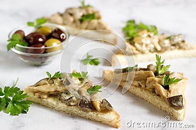 Triangular sandwiches with summer mushrooms cooked with cream and herbs served with olives. Stock Photo