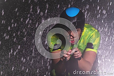 A triathlete braving the rain as he cycles through the night, preparing himself for the upcoming marathon. The blurred Stock Photo
