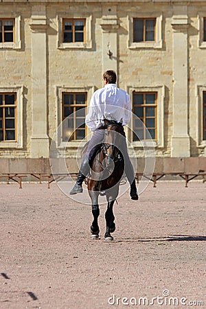 trick riding to men at bay stallion who jumps a trot on the sand square in front of the palace Editorial Stock Photo