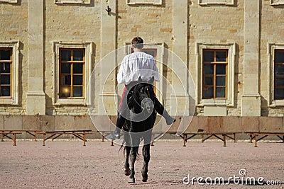 trick riding to men at bay stallion who jumps a trot on the sand square in front of the palace Editorial Stock Photo