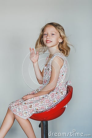 Cute European teen girl on a gray background sitting on a red chair. beautiful curly blonde with white teeth. an expressive smile Stock Photo