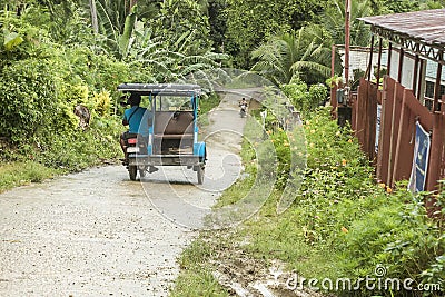 A tricycle goes downhill through a narrow single-lane concrete road. At a remote mountain barangay in Bohol, Philippines Editorial Stock Photo