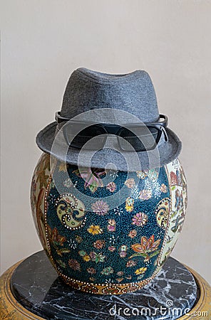 Trilby hat wearing sunglasses over antique decorated Chinese ceramic jar vase over antique black marble table Stock Photo