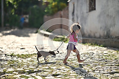 Trinidad, Cuba, August 16th, 2018: Little girl playing with her dog on the street of Trinidad Editorial Stock Photo