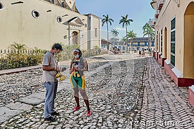 Adult Asian male tourist buying fresh bananas from local black woman on street in Trinidad, Cuba Editorial Stock Photo