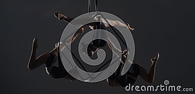 Trio of young female acrobats posing on a cube suspended at a height. Aerial gymnasts perform in studio against dark Stock Photo